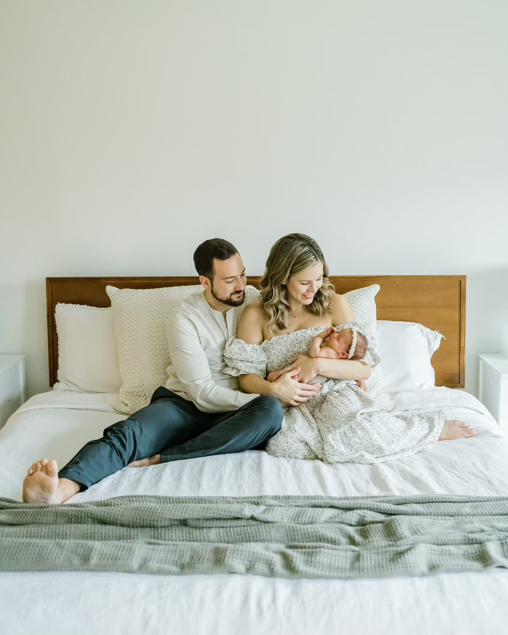 Man and woman sit on bed while holding newborn
