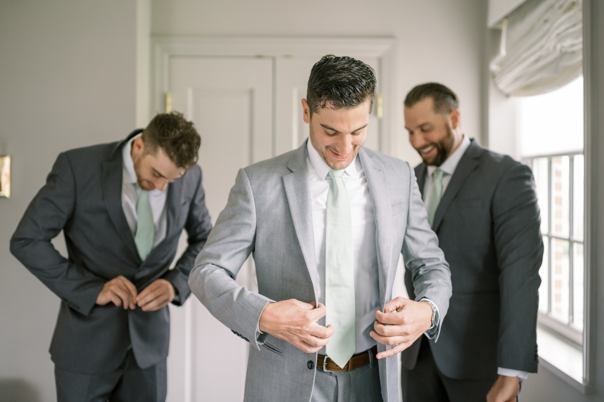 A groom puts on his wedding day suit with the help of his groomsmen.