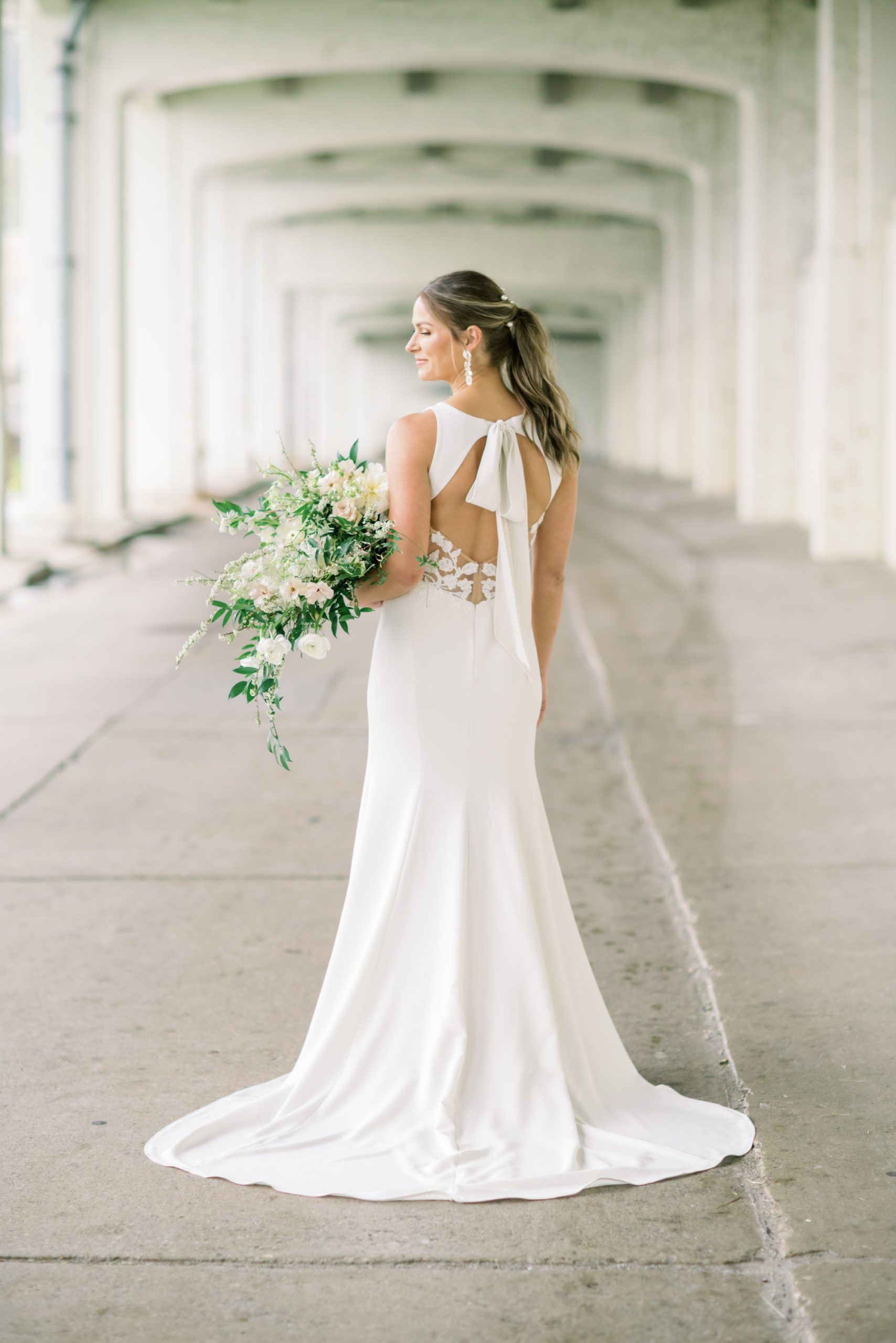 A bride poses with her back towards the camera while holding a gorgeous wedding bouquet