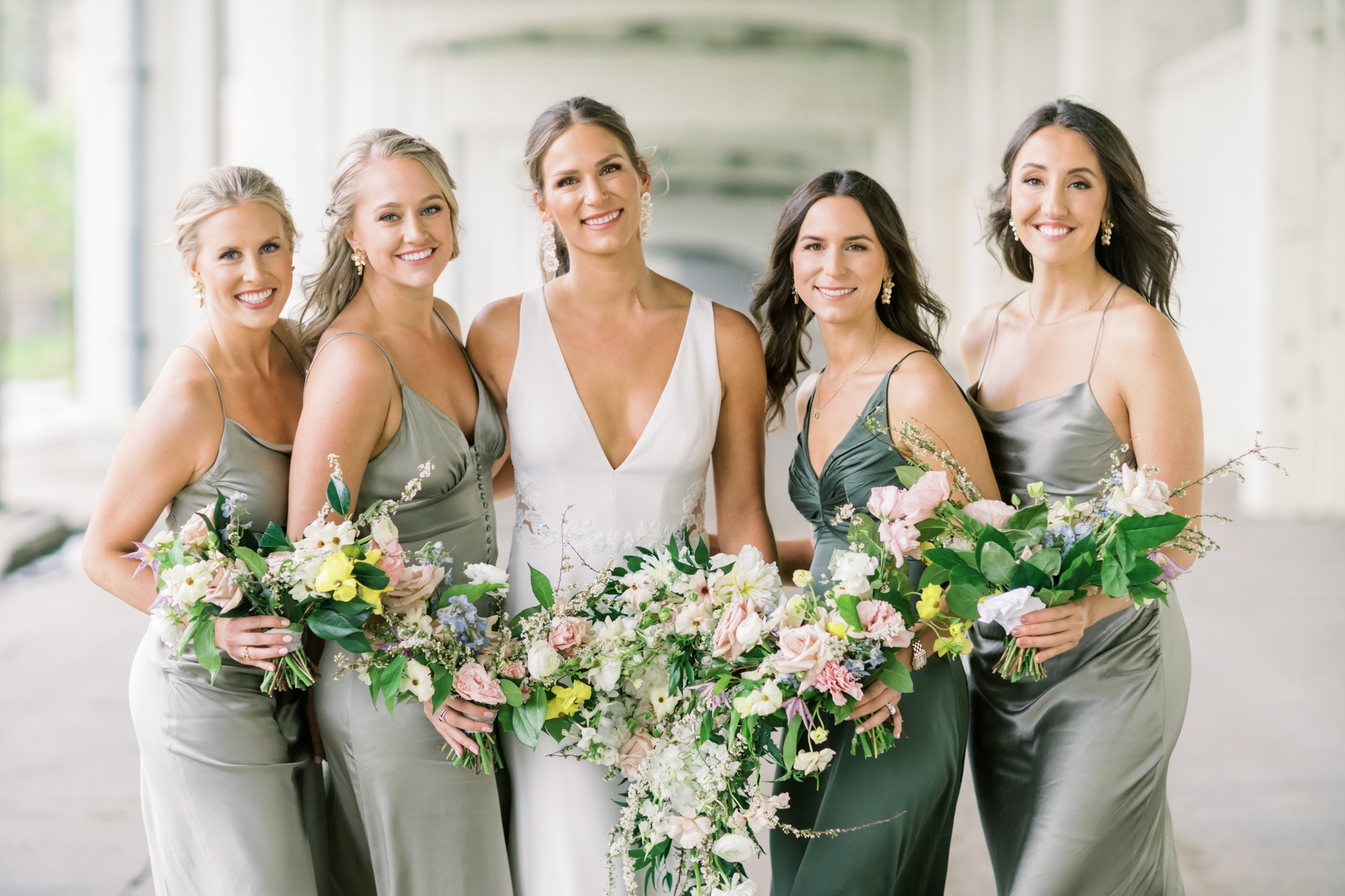 A bride poses with her four bridesmaids that are all wearing green satin bridesmaids' dresses