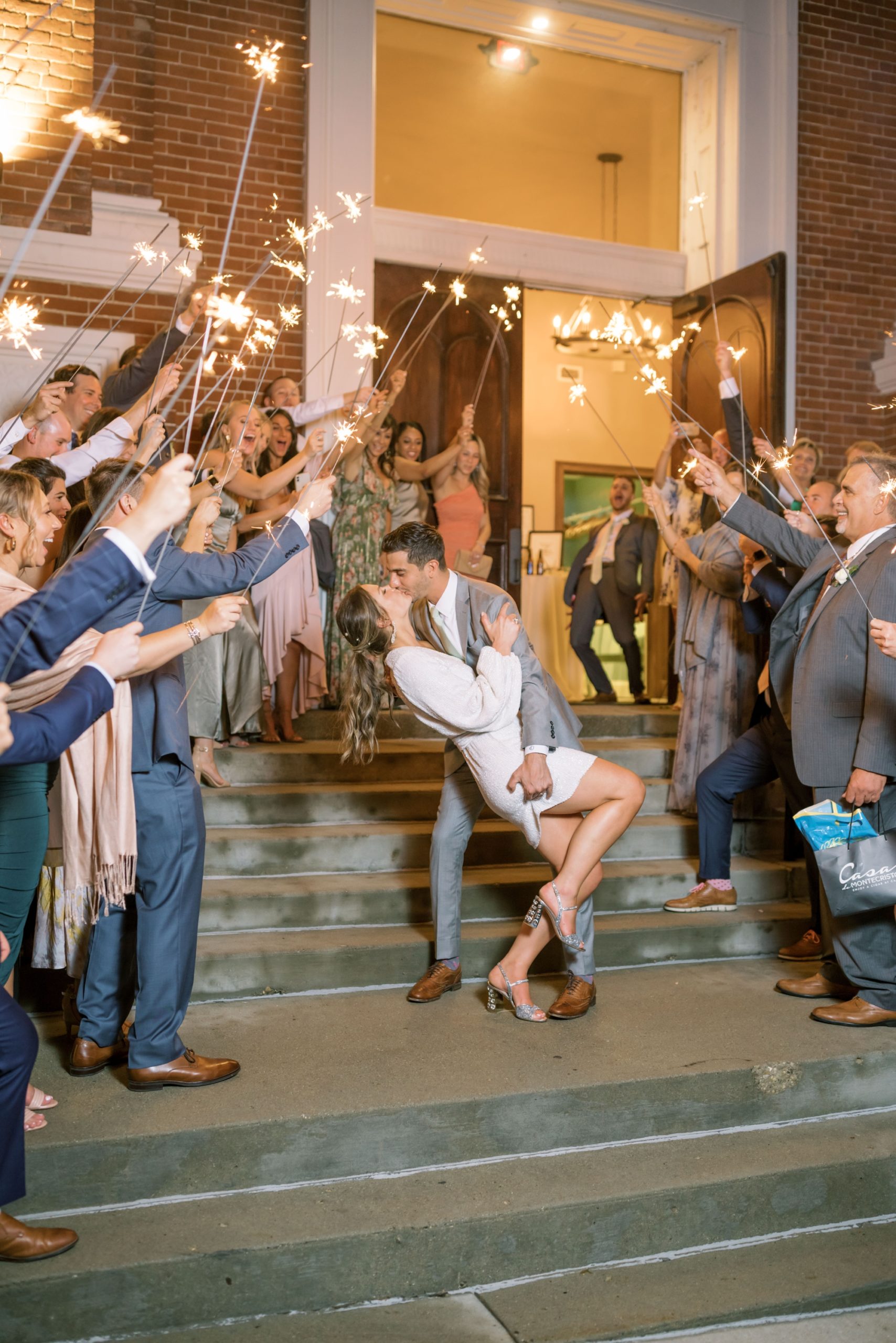 Photo of a bride and groom exiting their wedding while their guests hold sparklers for the sparkler send-off.