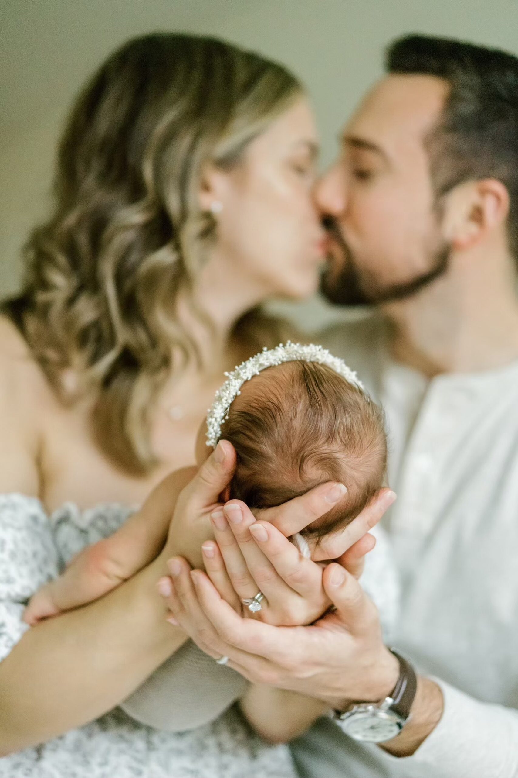 Man and woman kiss while holding newborn baby